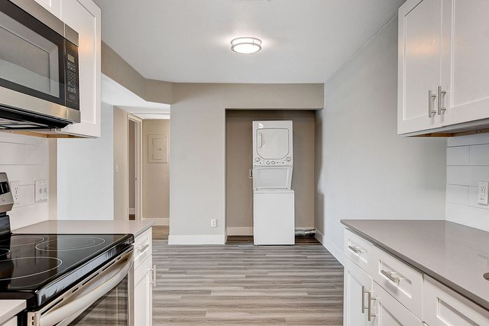 Modern kitchen with sleek appliances, bright white cabinetry, and an in-unit stacked washer-dryer in a spacious, well-lit layout.
