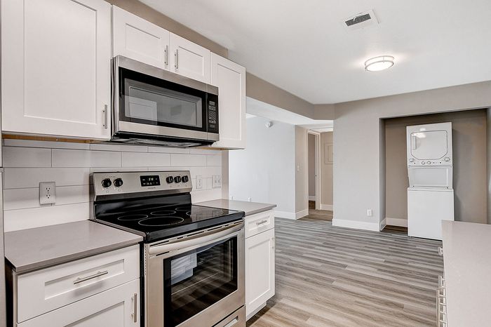Modern kitchen featuring sleek white cabinetry, stainless steel appliances, and elegant wood flooring, with a convenient in-unit washer and dryer.