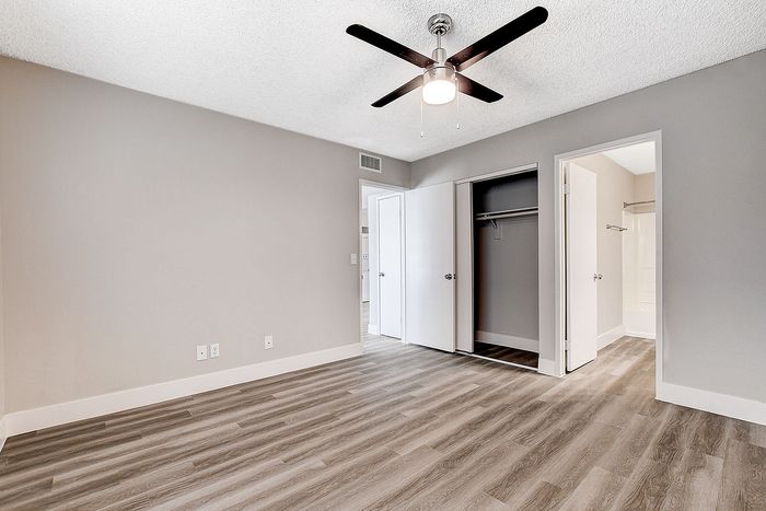 Bright bedroom with modern ceiling fan, spacious closet, and elegant wood flooring, perfect for stylish living.
