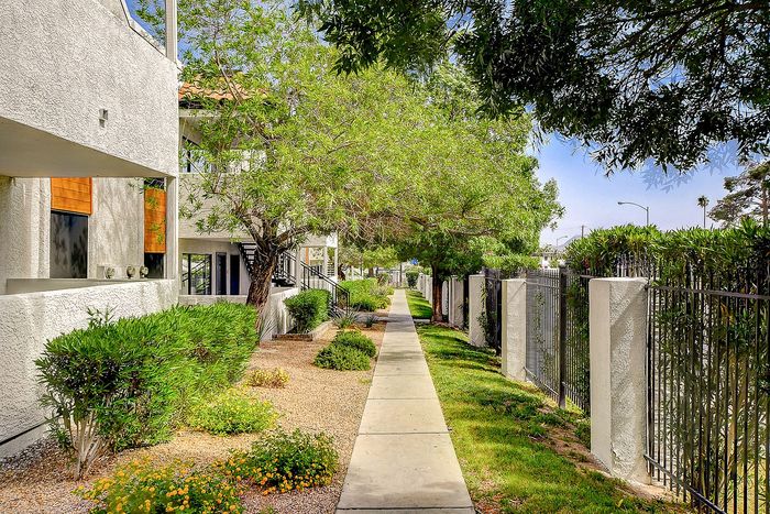 Charming walkway lined with lush greenery and modern apartment buildings, offering a serene and inviting atmosphere.