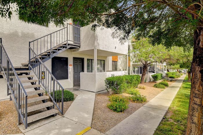 Charming apartment exterior with lush greenery and inviting stair entry, nestled in a peaceful residential community.