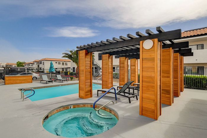 Inviting apartment complex pool area with modern wooden pergola, lounge chairs, and refreshing hot tub, perfect for relaxation and leisure.