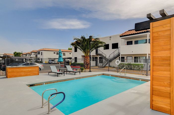 Inviting apartment complex with a sunlit pool, surrounded by palm trees and modern architecture, perfect for relaxation and leisure.