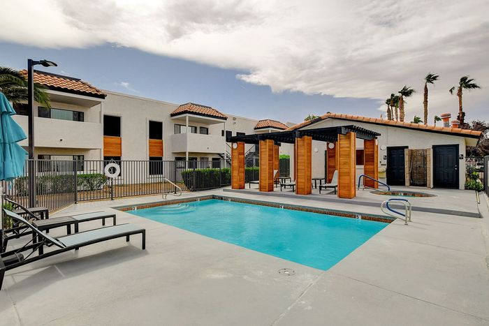 Inviting apartment complex featuring a modern swimming pool, stylish pergola, and Mediterranean-style architecture under a serene sky.
