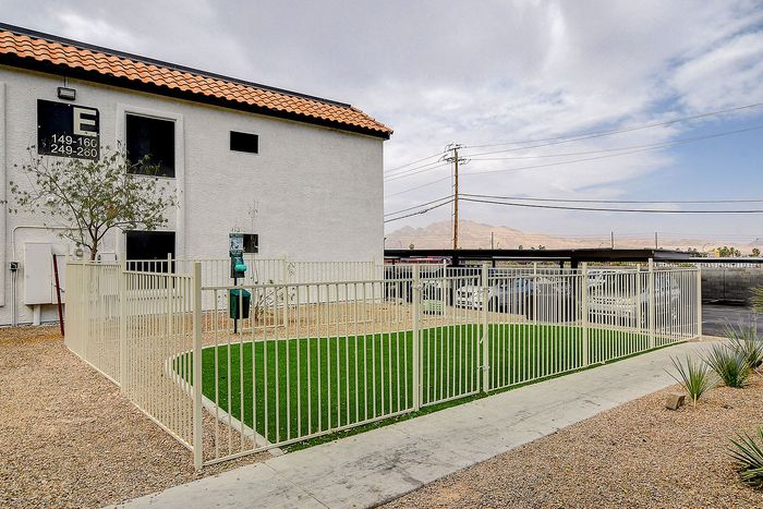 Charming apartment exterior with a well-maintained lawn and secure gated entry, offering mountain views and ample parking.