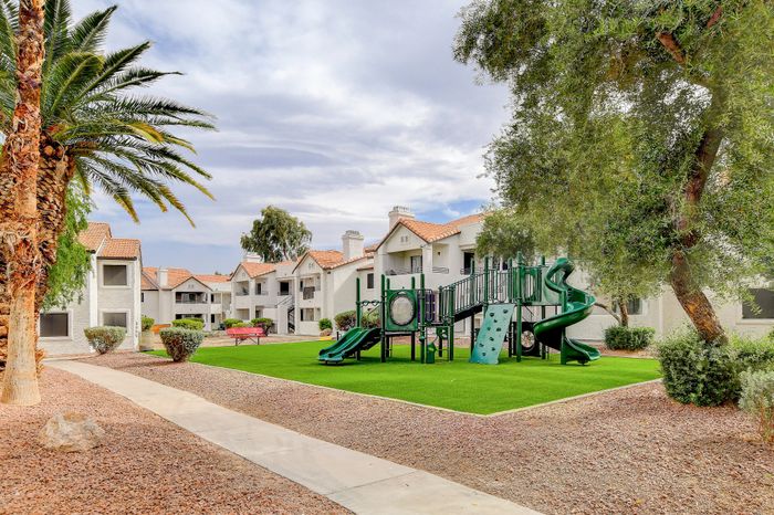 Inviting apartment complex with charming Spanish-style roofs, lush greenery, and a modern playground for family enjoyment.