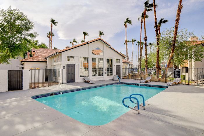 Inviting outdoor pool area with cozy lounge chairs, surrounded by tall palm trees and a charming building with large windows.