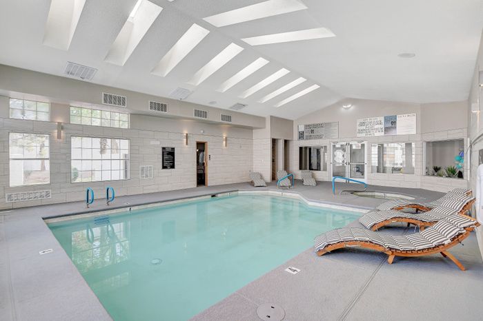 Elegant indoor swimming pool area featuring skylights and modern lounge chairs, perfect for relaxation and leisure.