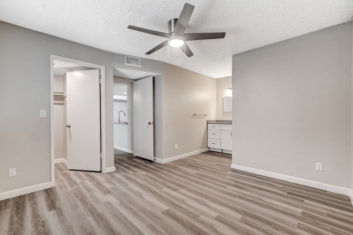 Modern bedroom with sleek hardwood flooring, ceiling fan, and stylish vanity area, perfect for comfort and relaxation.