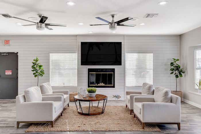 Bright, modern living room featuring cozy white armchairs, sleek ceiling fans, and a stylish fireplace, complemented by lush green plants.