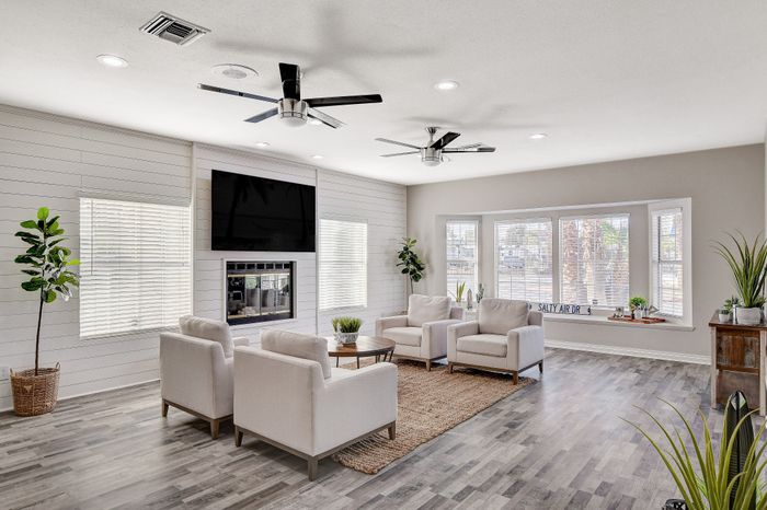 Elegant living room with large windows, modern ceiling fans, and cozy seating arrangement. Features stylish decor and ample natural light for a welcoming ambiance.