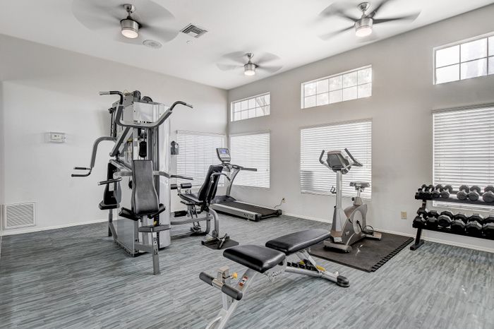 Modern fitness center with state-of-the-art equipment, including a treadmill, dumbbells, and multi-station gym machine, in a well-lit room with ceiling fans.