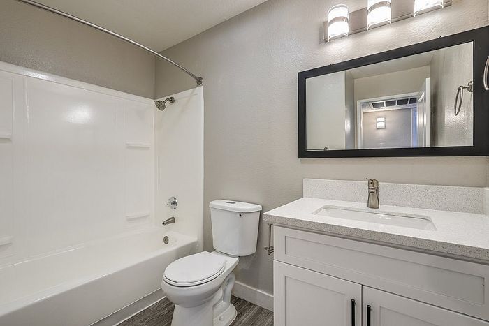 Modern bathroom with sleek white fixtures, featuring a bathtub, toilet, elegant vanity with a quartz countertop, and a large framed mirror under stylish lighting.