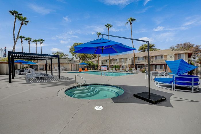 Inviting apartment community with a sparkling pool, hot tub, and stylish lounge areas under vibrant blue umbrellas.