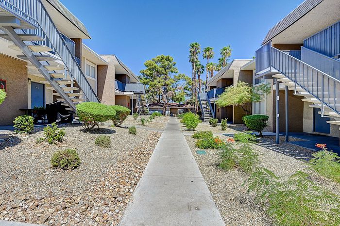 Inviting apartment complex with modern multi-story buildings, beautifully maintained landscaping, and a sun-drenched pathway leading to the entrance.