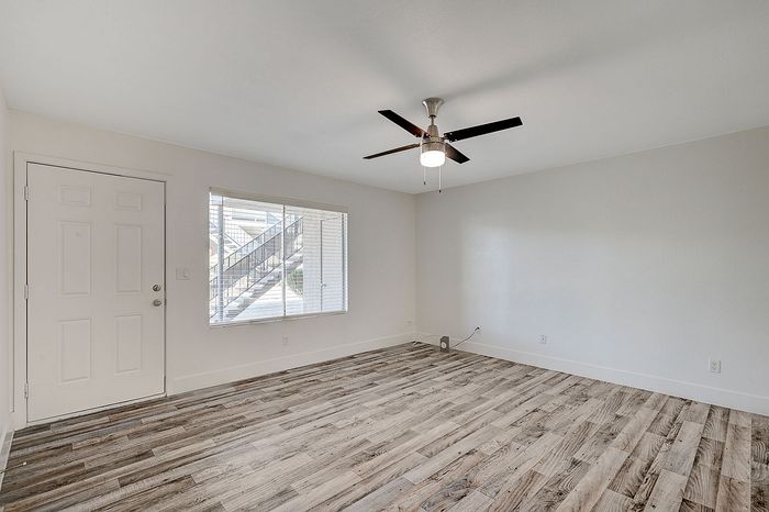 Bright and spacious living room with elegant wood flooring, modern ceiling fan, and a large window offering natural light.