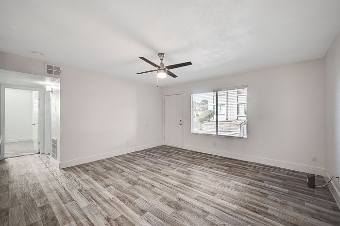 Bright and airy living room featuring elegant wood flooring, modern ceiling fan, and large window for natural light.