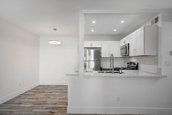 Modern kitchen with stainless steel appliances, sleek white cabinetry, and open dining area featuring stylish pendant lighting.