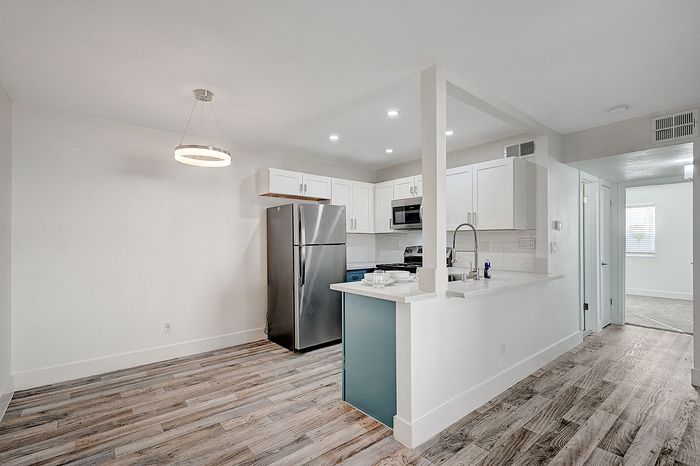 Modern apartment kitchen with sleek stainless steel appliances, bright white cabinetry, and elegant wood flooring.