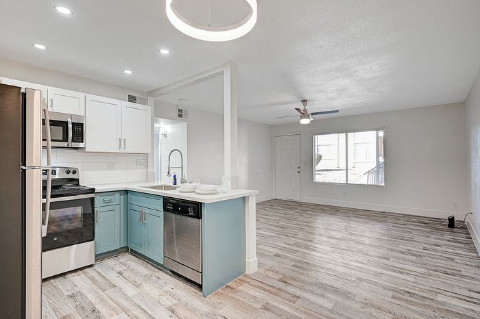 Beautiful open-plan kitchen and living area with modern lighting, stainless steel appliances, and stylish wood flooring.