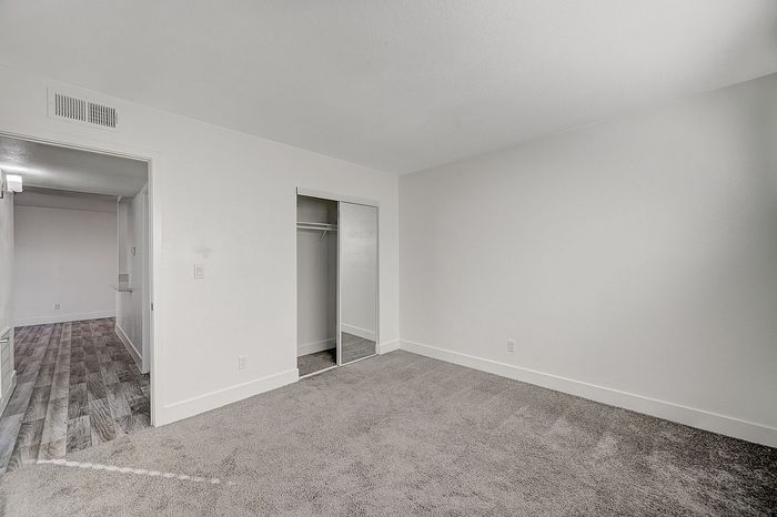 Spacious bedroom with plush carpeting and mirrored closet doors, leading to a stylish hallway with modern flooring.