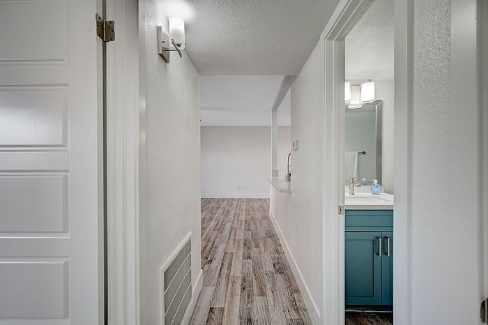 Inviting hallway with modern wood flooring leading to an elegant, open living space and a bathroom with chic cabinetry.