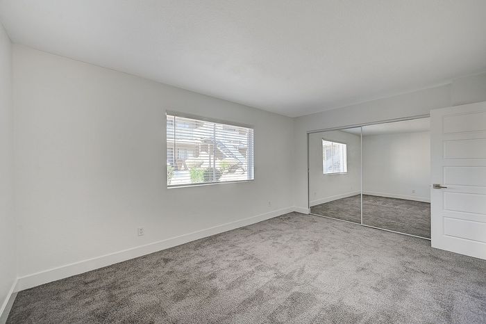 Bright and airy bedroom with plush carpet, mirrored closet doors, and large window offering abundant natural light.