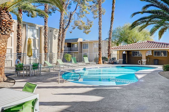 Inviting outdoor pool area with modern lounge chairs, surrounded by lush palm trees and stylish apartment buildings.