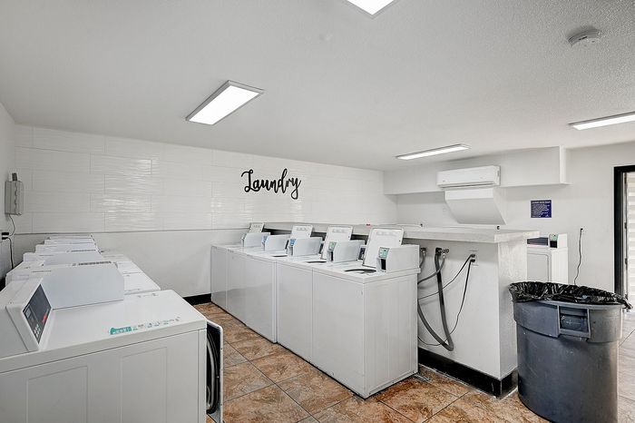 Bright and spacious laundry room equipped with multiple modern washing machines, featuring elegant tiled flooring and a welcoming atmosphere.
