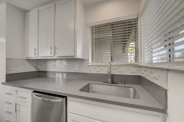 Sleek, modern kitchen with elegant white cabinets and sparkling granite countertops, featuring a large window with stylish blinds.