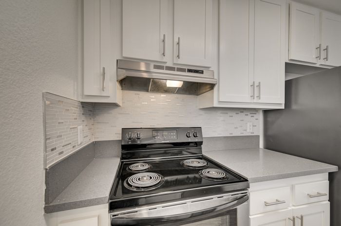 Modern kitchen with sleek black stove, stainless steel range hood, and elegant white cabinetry, complemented by a stylish mosaic tile backsplash.