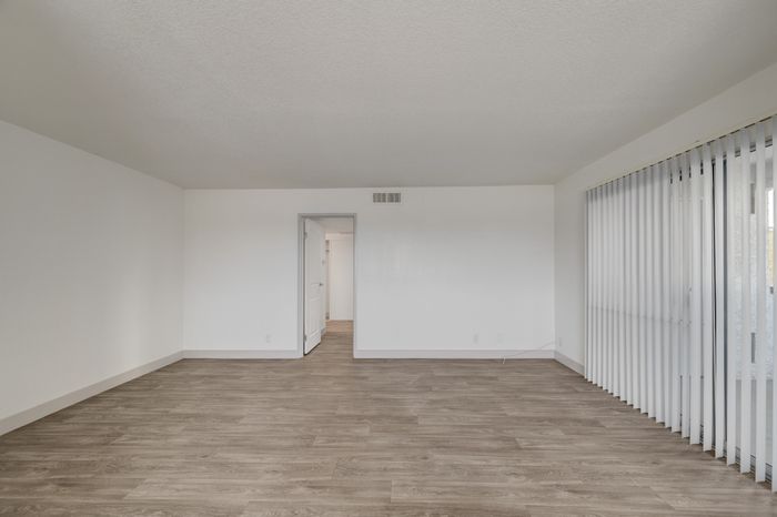 Bright and spacious living room with sleek hardwood floors and large sliding glass doors leading to a serene outdoor view.
