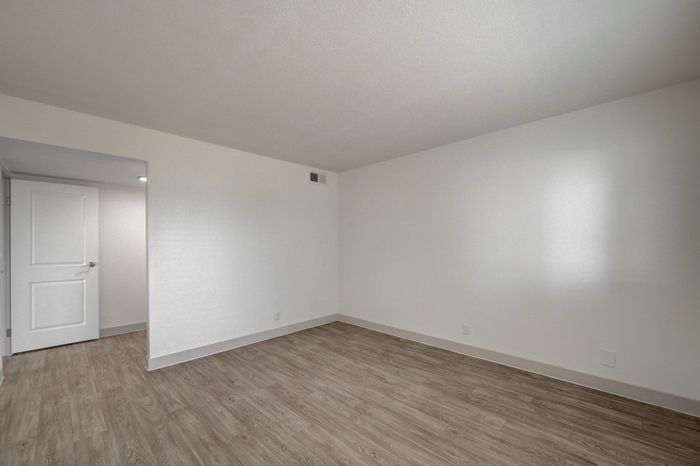 Bright and spacious room featuring modern wood flooring, fresh white walls, and ample natural light through the doorway.