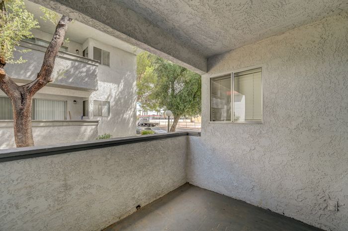 Charming apartment balcony with textured walls and a serene view of lush trees.