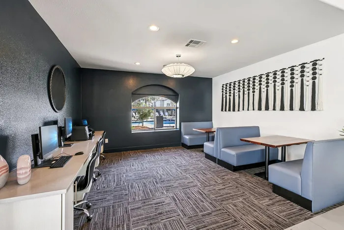 Modern shared workspace featuring sleek computer stations, stylish blue seating booths, and contemporary wall art.