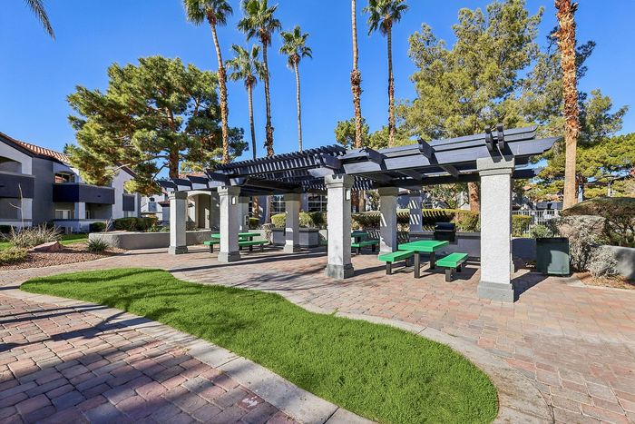 Charming outdoor patio with lush greenery and pergola, perfect for relaxation in a serene apartment community setting.