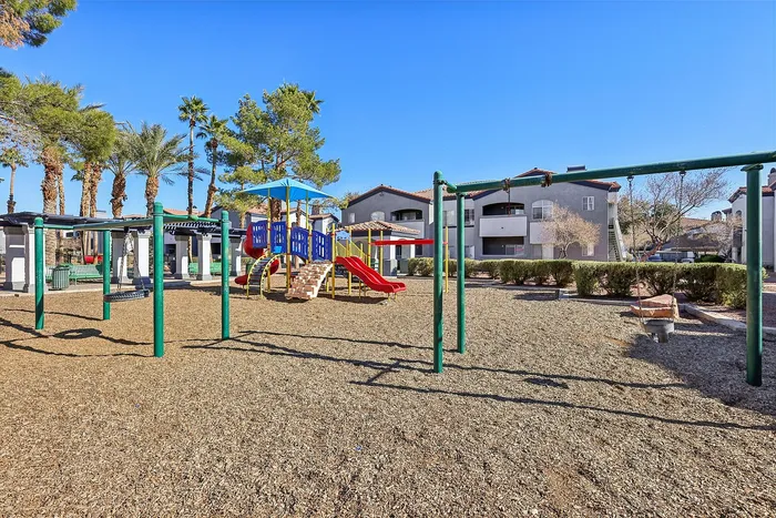 Inviting playground with colorful slides and swings, surrounded by lush greenery and palm trees, offering a vibrant community space in front of charming apartment buildings.
