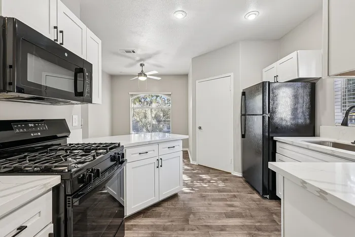Modern kitchen with sleek black appliances, white cabinetry, and large windows offering natural light.