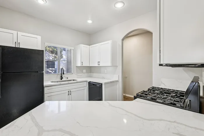 Modern kitchen with sleek white cabinetry, elegant black appliances, and pristine marble countertops, offering a bright and inviting cooking space.