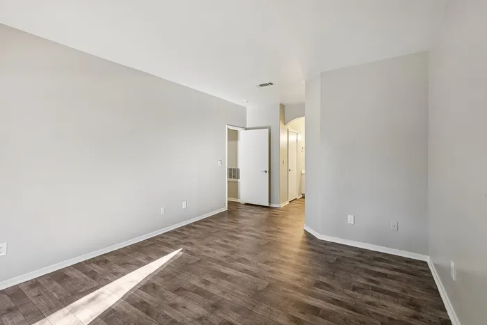 Bright and spacious room with elegant wood flooring and neutral walls, leading to an open doorway and a cozy hallway.