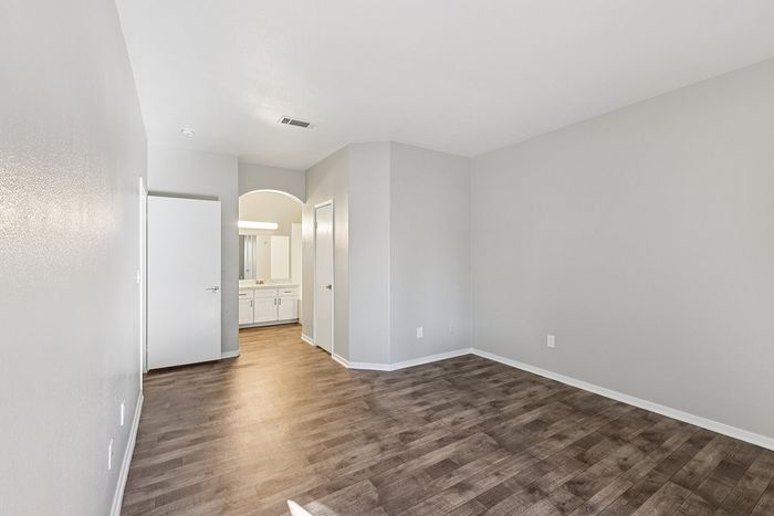 Modern apartment room with sleek hardwood floors and elegant gray walls, featuring a well-lit bathroom view.