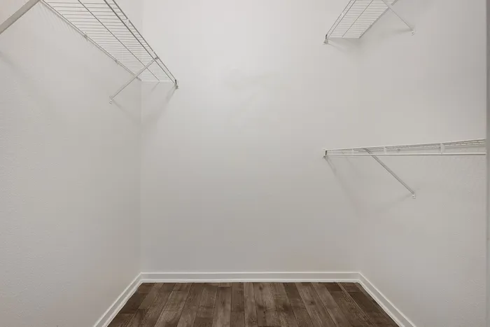 Spacious walk-in closet with elegant shelving and sleek hardwood flooring, offering ample storage options.