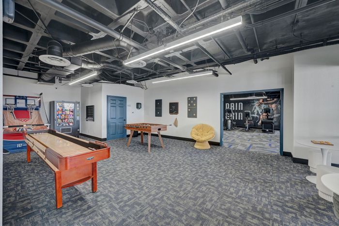 Vibrant recreation room with shuffleboard, foosball table, and indoor basketball hoop, adjacent to a modern fitness area.