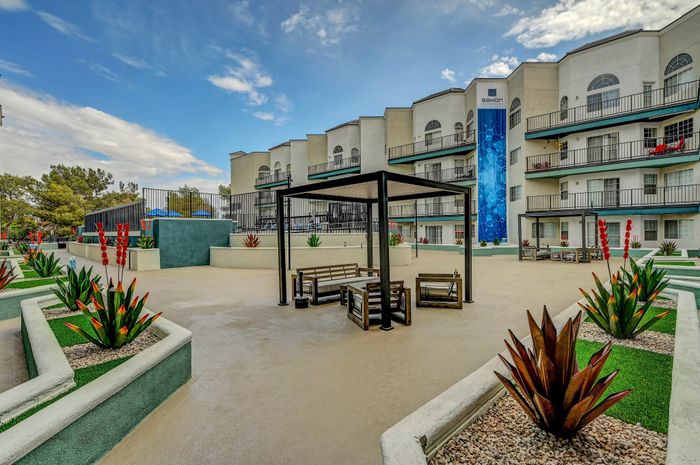 Modern apartment complex exterior featuring stylish outdoor seating and vibrant landscaping under a clear sky.