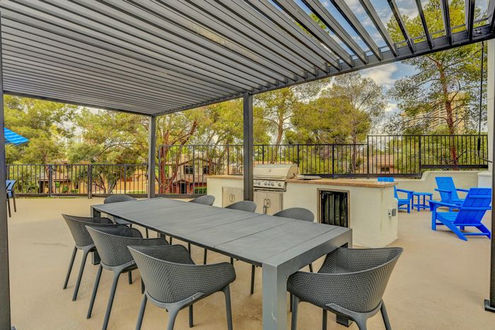 Inviting outdoor patio with a modern pergola, sleek dining set, and built-in grill, surrounded by lush greenery.