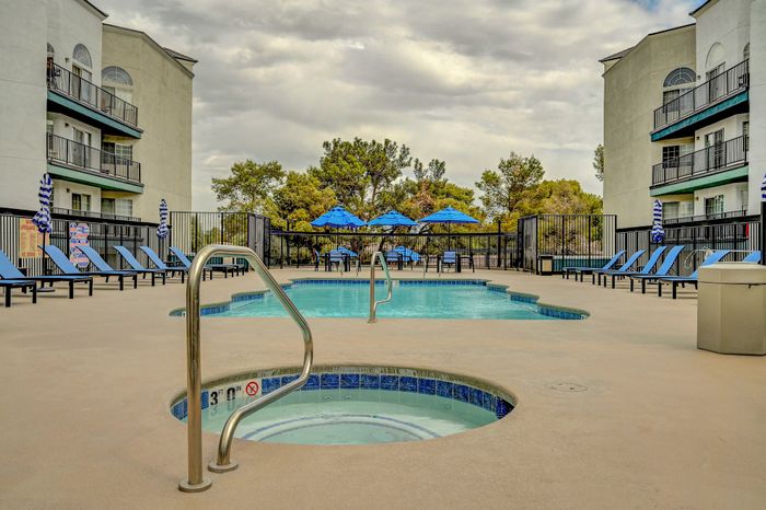 Contemporary apartment pool area with inviting loungers, vibrant umbrellas, and lush greenery backdrop.