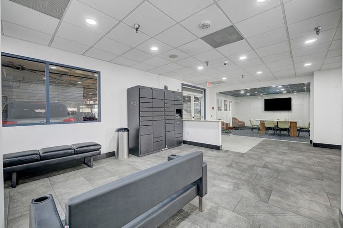 Contemporary apartment lobby with sleek design, featuring a parcel locker, seating area, and spacious conference room behind glass walls.
