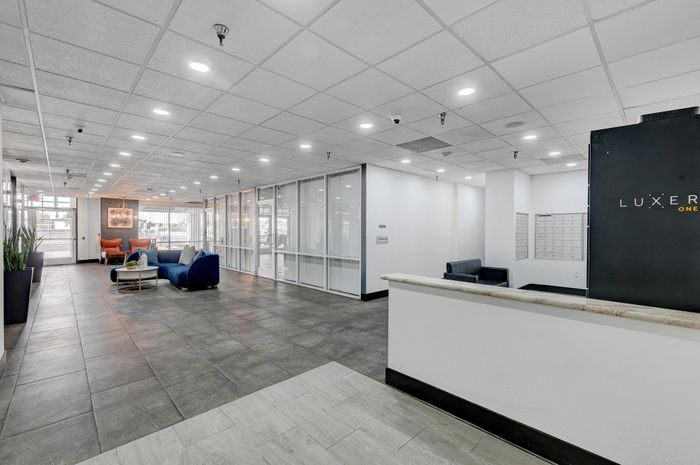 Modern and inviting apartment lobby with sleek tile flooring, chic blue seating area, and ambient lighting. Glass panel walls create a spacious and airy atmosphere.