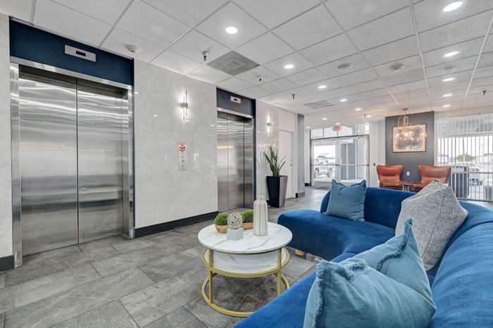 Chic apartment lobby showcasing modern elevators, sleek marble walls, and stylish seating area with blue velvet sofa and elegant decor.