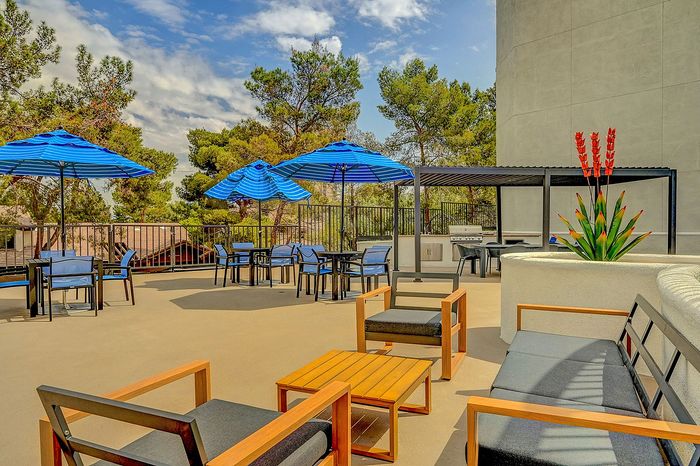 Inviting outdoor patio with modern seating, vibrant blue umbrellas, and a grill area, surrounded by lush greenery.
